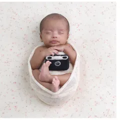 For the future photographer. A simple swaddled pose with a cute felt camera prop, adding a touch of personality to a classic newborn shot.