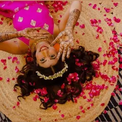 A creative shot of a beautiful bride lying amidst rose petals, her henna-adorned hands framing her happy face.