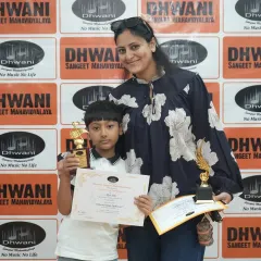 A mother proudly stands with her son, who is holding his awards from the Dhwani Kala Mahotsav. Our prize ceremony is a family affair, celebrating student success together.