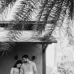 A quiet and intimate black and white portrait under the shade of palm leaves. This photo has a beautiful, gentle quality, focusing on the couple's peaceful connection.