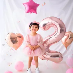 Two looks so good on her! This birthday girl is standing proud next to her giant number '2' balloon, surrounded by a sea of pink and rose gold.