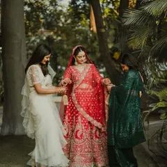 A bride in her red lehenga shares a moment with her bridesmaids, who are helping her with her kalire.