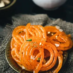 A plate of hot, crispy, and syrupy jalebis. I used a dark, moody style to make the bright orange color of the dessert stand out.