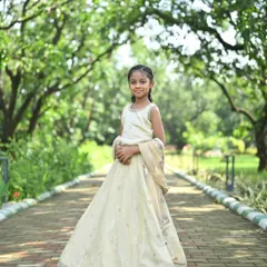 A full-length shot of a young girl in our off-white kids' lehenga, looking absolutely angelic in a beautiful park.