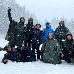 Our group of happy trekkers, clad in ponchos, enjoying a fresh snowfall at Juda Ka Talab campsite during the Kedarkantha trek. These are the moments of pure, unadulterated joy.