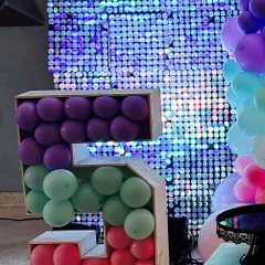 A creative number "5" prop filled with purple, green, and red balloons, set against a sparkling blue shimmer wall for a fun birthday party.