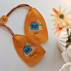 A pair of mustard yellow leather keychains, each featuring a hand painted camel and personalized with the names 'Tani' and 'Poddar'. The warm colors and artistic touch make these truly special.