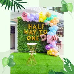 Celebrating the halfway mark to one year is a milestone in itself. This "Half Way to One" setup for a 6 month birthday featured a fun candy theme with bright pastel balloons and gold foil letters against a green hedge backdrop.
