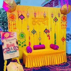 An outdoor Haldi and Mehendi setup with a bright yellow backdrop and traditional hangings. I included a custom welcome sign on an easel to greet guests, and the seating area is accented with Rajasthani umbrellas for a festive feel.