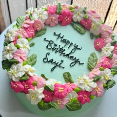 Another perspective of the "Happy Birthday Sayi" cake, showing the delicate arrangement of the buttercream flowers and leaves. We take care to make our cakes beautiful from every angle.