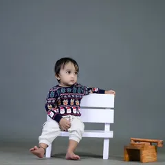 A cool and casual pose from a little boy on a white bench. The simple grey background creates a classic, timeless look.