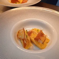 A delicate pasta dish featuring two pieces of agnolotti filled with a savory mixture, garnished with crispy prosciutto.