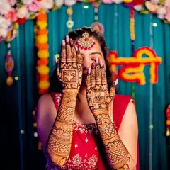 A happy bride showing off her intricate wedding mehndi. This design features personalized blocks on the palms with full geometric and floral patterns extending up the arms.
