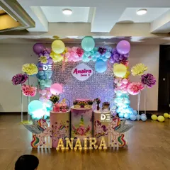 A unicorn-themed party for Anaira's 4th birthday. The decor includes a shimmering silver sequin backdrop, pastel balloon arrangements, large paper flowers, and unicorn props with light-up letters.