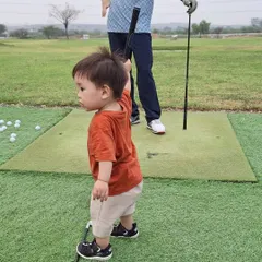 It is never too early to start. This little one is already getting a feel for the game, holding a golf club on the green with his father nearby.
