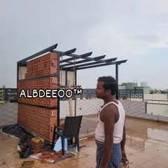A wider view of the pergola structure during construction. The combination of the modern black MS frame and the earthy, patterned terracotta wall creates a unique and stylish aesthetic right from the build stage.