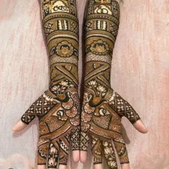 Symmetry and sharpness are obsessions for me. This full-arm bridal mehendi features perfectly mirrored peacocks and architectural jharokha patterns, showing the 'baariki' or fine detailing that I am known for.