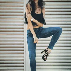 A classic fashion pose that highlights the fit of the skinny jeans and the strappy heels. The simple background keeps the focus entirely on the model and the brand's apparel.