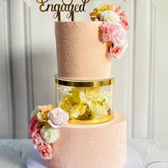 This floating tier engagement cake creates a beautiful illusion. The clear separator is filled with soft yellow flowers, connecting the two blush-pink tiers that are finished with a delicate stencil pattern and fresh floral arrangements.