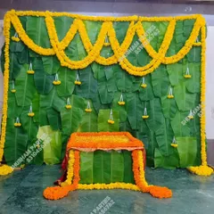 A classic and vibrant backdrop for a traditional Indian ceremony, such as a puja or Simmanta. This decoration is made entirely of fresh banana leaves and decorated with beautiful marigold flower garlands, creating an authentic and auspicious setting.