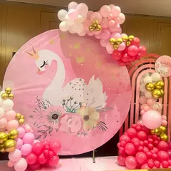 A simple and elegant swan-themed Aqeeqah ceremony. The decor features a large circular backdrop with a graceful swan graphic, surrounded by a pink, white, and gold balloon garland.