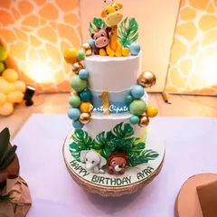 A close-up of the three-tiered safari cake for Ayra's first birthday. The adorable fondant animals and tropical leaves perfectly capture the 'Wild One' spirit.