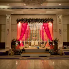 An elegant indoor wedding stage at the ITC Gardenia, featuring vibrant pink and orange drapes and beautiful floral arrangements.