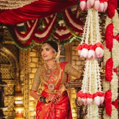 A close-up of the bride against the traditional mandap, highlighting the detailed floral work with lotus bud hangings and classic red and white garlands.