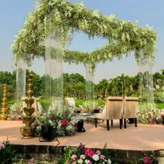 A full view of the modern acrylic mandap set against a serene lake. The transparent pillars give the illusion that the lush floral canopy is floating on air, creating a truly magical setting.