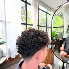 A view from the chair of the final permed hairstyle. The curls are well-defined, and the fade is blended perfectly.