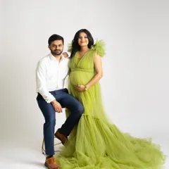 A bright and happy couple's portrait against a clean white background. The mother-to-be shines in a lime green tulle gown while her partner sits beside her, both smiling for the camera.