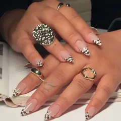 A stylish and trendy nude manicure taken to the next level. This image shows off the glossy finish of our cow print French tips, paired with chunky gold rings.
