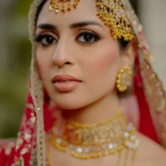 A portrait of bridal perfection. This close-up highlights the bride's flawless makeup and the exquisite detail of her traditional gold jewelry, including the jhoomar and tikka. It’s a celebration of the artistry that goes into the bridal look.