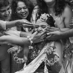 A black and white shot capturing the beautiful chaos of a Haldi ceremony, where the bride is lovingly covered in turmeric by her family.