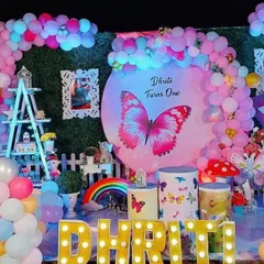 This colorful butterfly-themed first birthday shows a full stage setup with a rainbow of pastel balloons. It includes a personalized backdrop, themed plinths for the cake, and a life-sized cutout of the birthday girl.