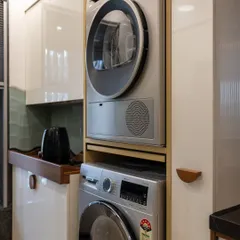 This custom cabinet neatly stacks a washer and dryer, making use of vertical space. This solution keeps the laundry appliances accessible but contained, maintaining the kitchen's clean and organized aesthetic.