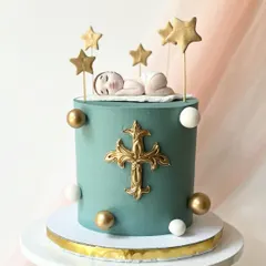 An elegant cake for a baptism or christening. It features a sleeping baby, a golden cross, and stars, all on a serene teal buttercream base.