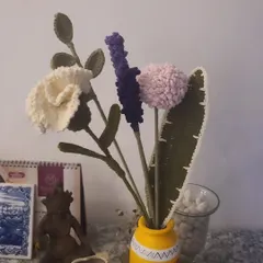 This is my first-ever full bouquet, featuring a mix of textures and colors. You can see a white carnation, purple lavender, and a pink pom-pom flower, each carefully crocheted. These are perfect for gifting or as a unique piece of home decor.