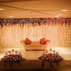 A curtain of warm fairy lights creates a magical and romantic backdrop for this reception stage. The simple sofa with bright cushions provides a pop of color, while the overhead floral runner adds a touch of natural beauty to the entire setup.