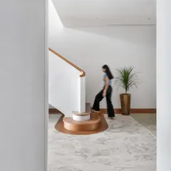 A view of the winding staircase, showing how its form guides movement and circulation between the two levels of the duplex apartment. The use of wood and soft curves adds warmth to the minimalist space.