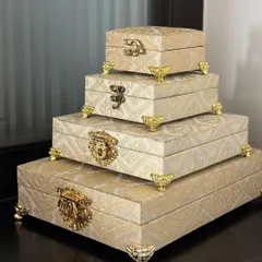 A stack of four nesting trousseau boxes in an elegant cream and gold brocade fabric. Featuring ornate metal clasps and feet, these are perfect for organizing everything from sarees to accessories.