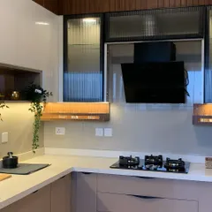 This kitchen design is all about vibrant color combinations and practical space utilization. The handleless cabinets, quartz countertop, and fluted glass shutters on the overhead units create a modern and functional cooking area.