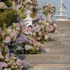 A magnificent floral installation on a grand staircase in Udaipur. A cascade of pastel pink, lavender, and white flowers creates a fairytale entrance for a wedding ceremony.