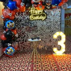 A classic Mickey Mouse theme for a 3rd birthday, featuring a silver shimmer wall, a red and black balloon arch with Mickey Mouse foil balloons, and a light-up number '3'.