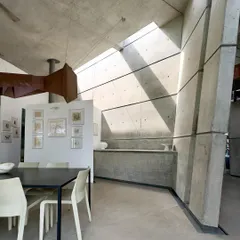 The dining area of the 'House of Stories' in Bangalore, where angled concrete walls and a skylight create a dramatic play of light. The space is designed to feel both monumental and intimate, a place for shared meals and quiet contemplation.