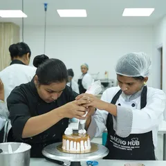 We believe in 100% hands-on learning. Here, I am guiding a student to perfect her piping technique on a caramel drip cake. You get personal attention to ensure you master every skill, from holding the piping bag correctly to creating beautiful, stable decorations.