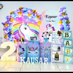 This magical unicorn theme for Kausar's second birthday is filled with rainbow colors and sparkle. The setup includes unicorn cutouts, a large marquee number '2', and a vibrant balloon arch over a rainbow backdrop.