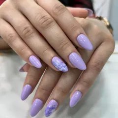 A beautiful, soft lavender polish on almond-shaped nails. The accent nail features a subtle, marbled design in shades of purple and white for a touch of artistry.