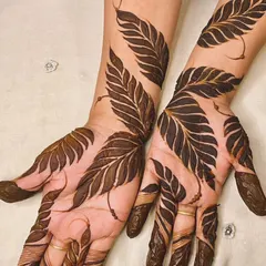 This is a perfect example of a bold Gulf-style henna design. The prominent, shaded leaf patterns create a striking contrast against the skin, flowing from the fingers up the arm for a modern and dramatic effect.