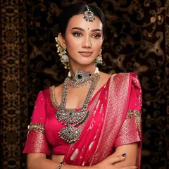 A close-up of the silver-finish oxidized jewellery, showing the intricate details and the contrast of the green stones against the dark pink saree.
